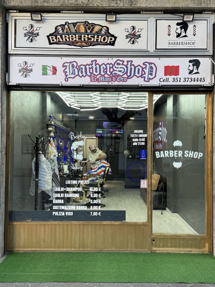 La vetrina del negozio con l'insegna BarberShop Le Mani d'Oro e il listino prezzi scritto sul vetro